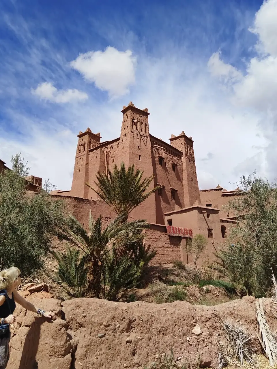 Earthen kasbah rising above palm trees under a blue sky